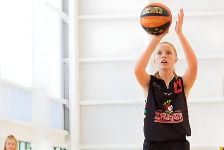 Eine junge Basketballspielerin der Wellington Point State High School springt in der Halle und erreicht den Ball.