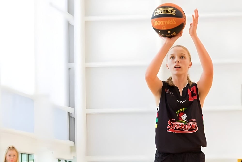 Eine junge Basketballspielerin der Wellington Point State High School springt in der Halle und erreicht den Ball.