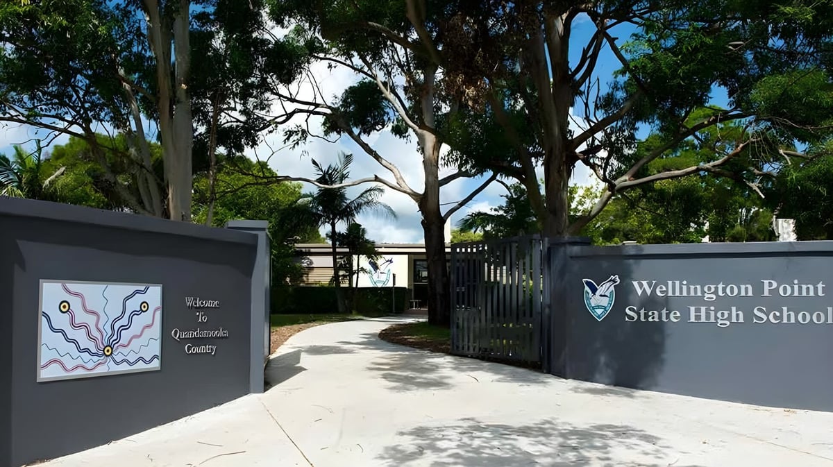 Der Eingang zur Wellington Point State High School mit dem Schulgebäudeschild und umgeben von Bäumen und Pflanzen.