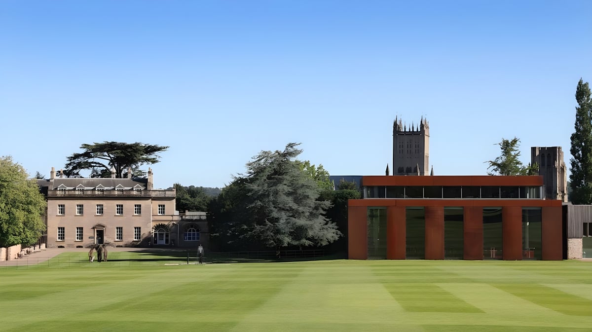 Der grüne Campus der Wells Cathedral School mit historischen Gebäuden und einem modernen Turm im Hintergrund bei blauem Himmel.