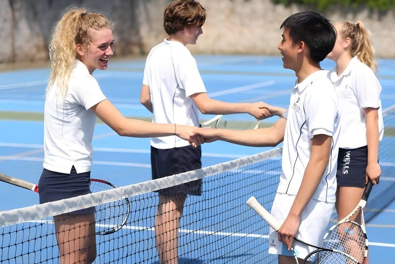 Schüler der Wells Cathedral School geben sich auf einem bunten Tenniscourt im Freien die Hand.