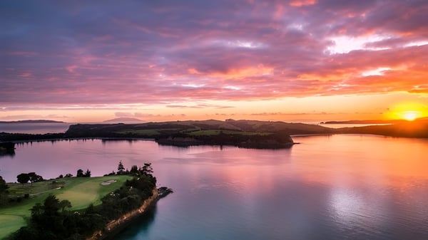 Ein Sonnenuntergang über einem ruhigen See mit grünen Hügeln auf dem Gelände von Wentworth College.