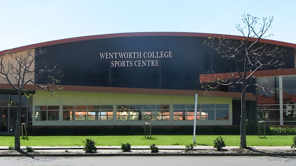 Das Wentworth College zeigt sein großes Sportzentrum mit geschwungenem Dach und umliegender Begrünung.