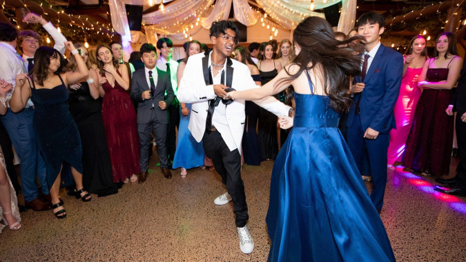 Schüler und Lehrer des Wentworth College tanzen bei einer festlichen Veranstaltung in einem dekorierten Saal.