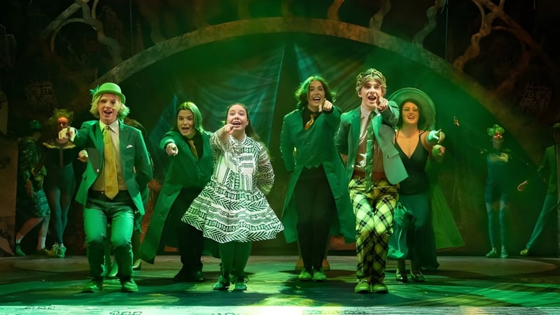 Eine Gruppe von Schülerinnen und Schülern des Wesley College führt auf der Bühne vor einem grünen Hintergrund ein Kostümstück auf.