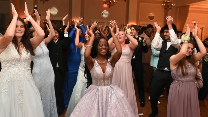 Eine Gruppe von Menschen feiert gemeinsam unter einem Kronleuchter im festlichen Gebäude des Wesley College.