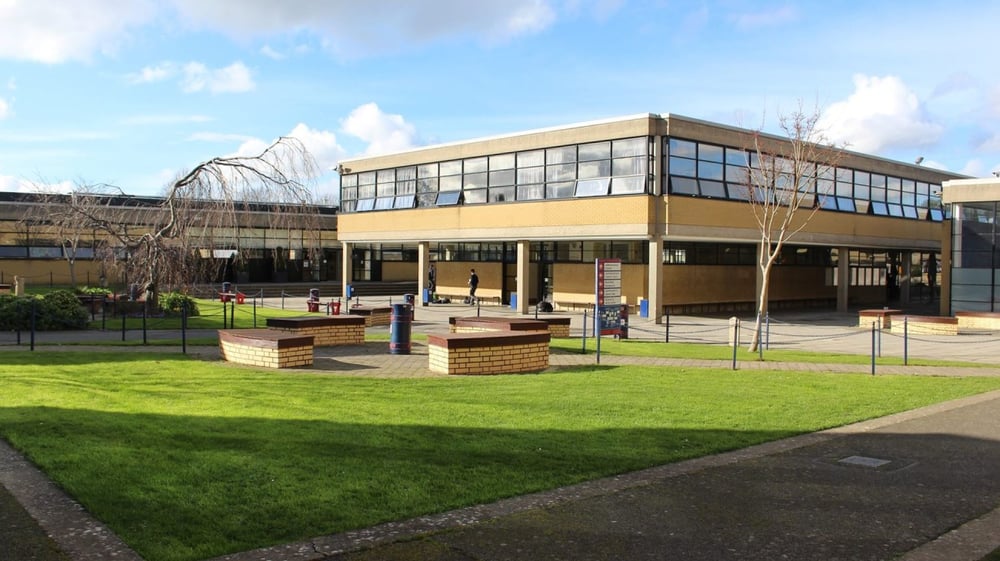 Das moderne mehrstöckige Gebäude mit gelber Fassade auf dem Campus des Wesley College steht in einer grasbewachsenen Anlage mit Sitzbänken.