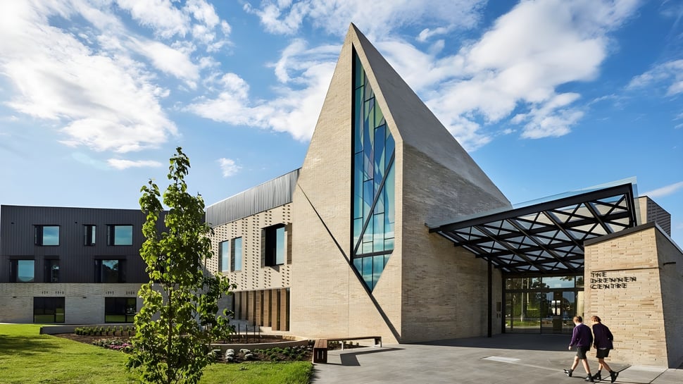 Ein modernes Gebäude mit Glasfassade steht auf dem Campus des Wesley College, umgeben von Grünflächen und Bäumen.