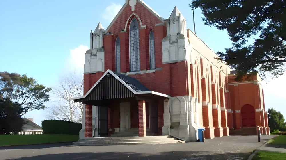 Die rote Backsteinkirche mit gotischer Architektur steht auf dem Campus des Wesley College und wird von Bäumen umgeben.