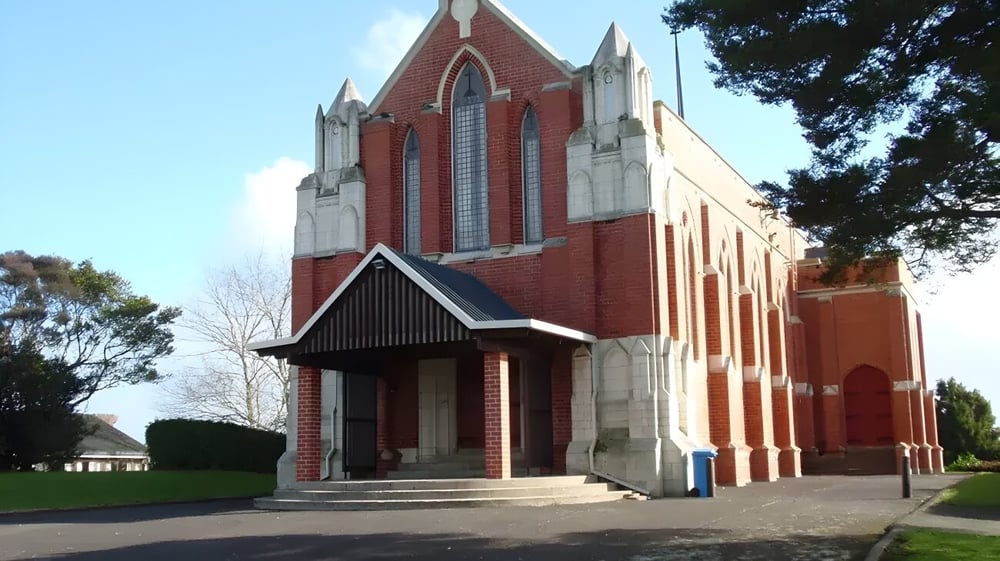 Eine große Ziegelkirche mit hohem Turm steht auf dem Gelände des Wesley College, umgeben von Gras und Bäumen.