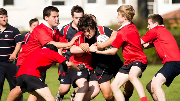 Schüler des Wesley College sind in roten und schwarzen Sportuniformen auf einem Sportfeld in einer körperlichen Aktivität zu sehen.