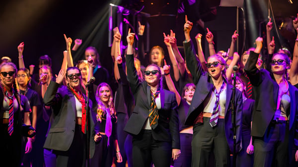 Eine Gruppe von Schülerinnen und Schülern der West Buckland School steht auf der Bühne mit erhobenen Armen unter buntem Licht.