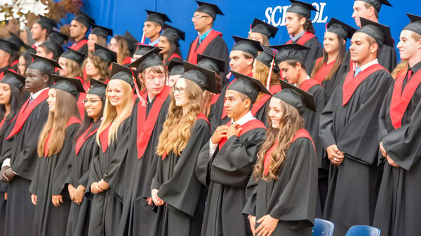 Eine große Gruppe Absolventen der West Carleton Secondary School steht in schwarzen Roben und roten Stolen vor einem blauen Hintergrund mit dem Schullogo.