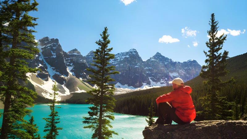 Eine Person in roter Jacke sitzt auf einem Felsen mit Blick auf einen türkisfarbenen See umgeben von schneebedeckten Bergen auf dem Gelände der West Carleton Secondary School.