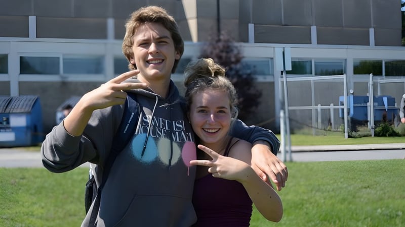 Zwei Schülerinnen und Schüler der West Carleton Secondary School stehen auf einer Wiese vor einem Schulgebäude und machen verspielte Gesten.