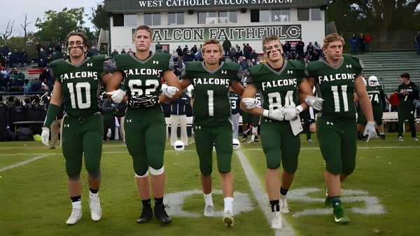 Eine Gruppe von Football-Spielern in grünen und weißen Trikots steht auf dem Spielfeld im West Catholic High School Stadion.