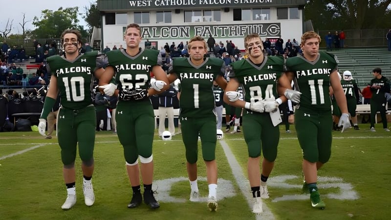 Eine Gruppe von Football-Spielern in grünen und weißen Trikots steht auf dem Spielfeld im West Catholic High School Stadion.