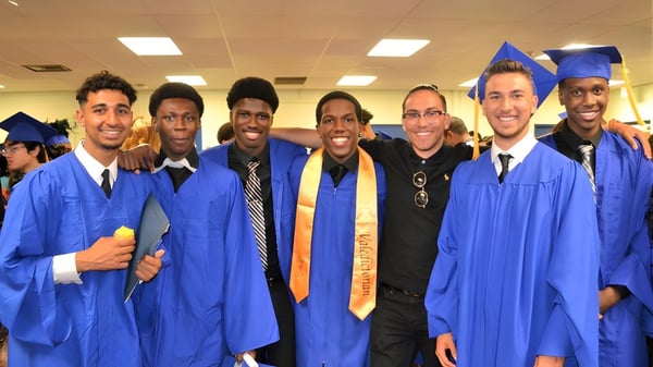 Eine Gruppe von Absolventen posiert in blauen Abschlussgewändern und Hüten auf dem Campus des West Humber Collegiate Institute.