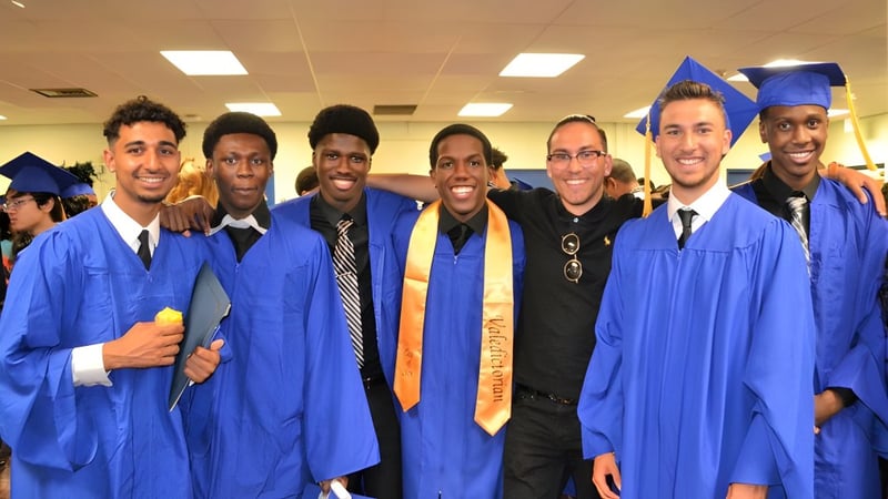 Eine Gruppe von Absolventen posiert in blauen Abschlussgewändern und Hüten auf dem Campus des West Humber Collegiate Institute.