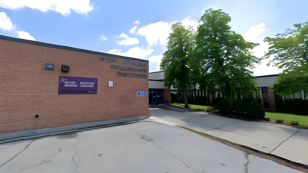Das Backsteingebäude des West Humber Collegiate Institute ist von Bäumen umgeben und steht an einem gepflasterten Weg.
