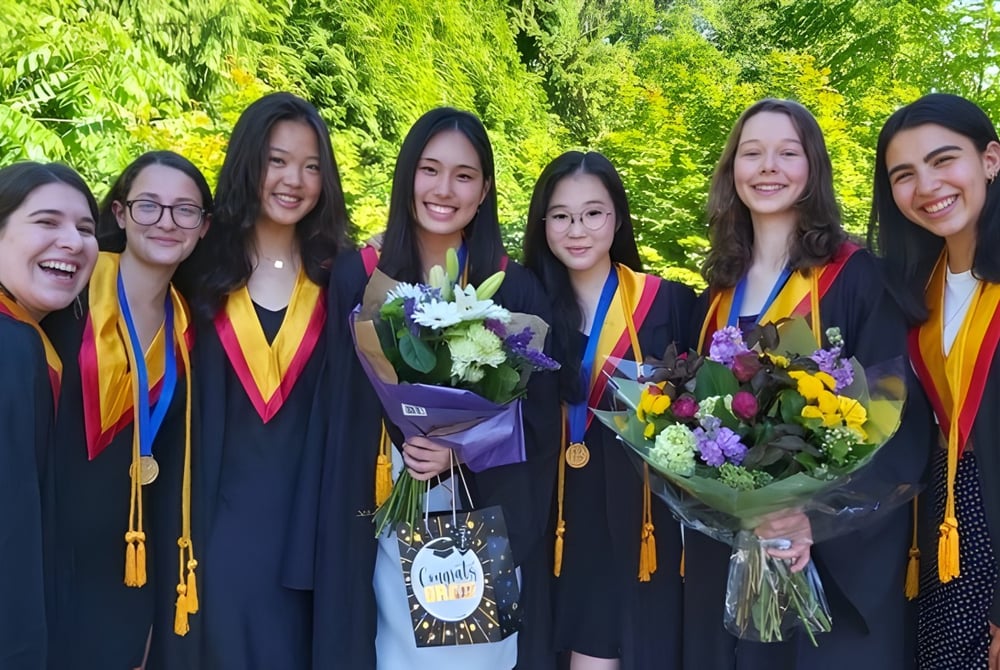Eine Gruppe von Absolventinnen der West Vancouver Secondary steht mit Blumensträußen vor grünem Hintergrund.