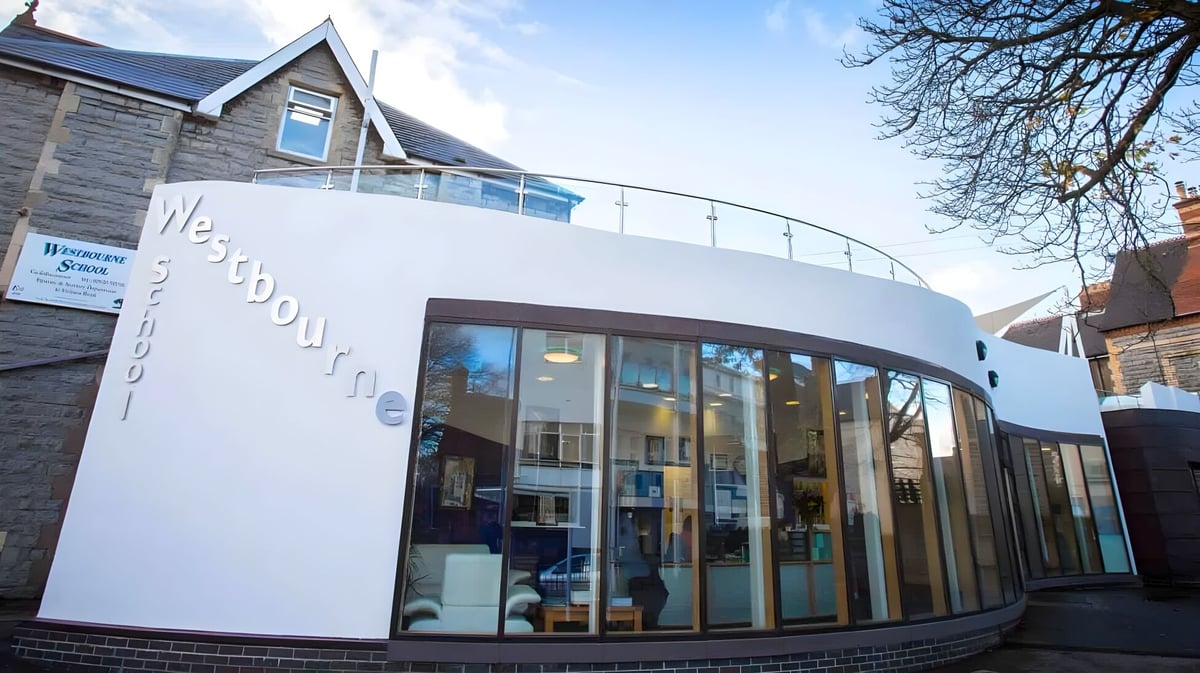 Das moderne Gebäude der Westbourne School mit einer Glasfassade steht vor Bäumen unter klarem Himmel.