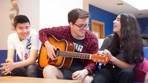Drei Schüler der Westbourne School sitzen zusammen, ein Schüler spielt akustische Gitarre, die anderen beiden unterhalten sich.