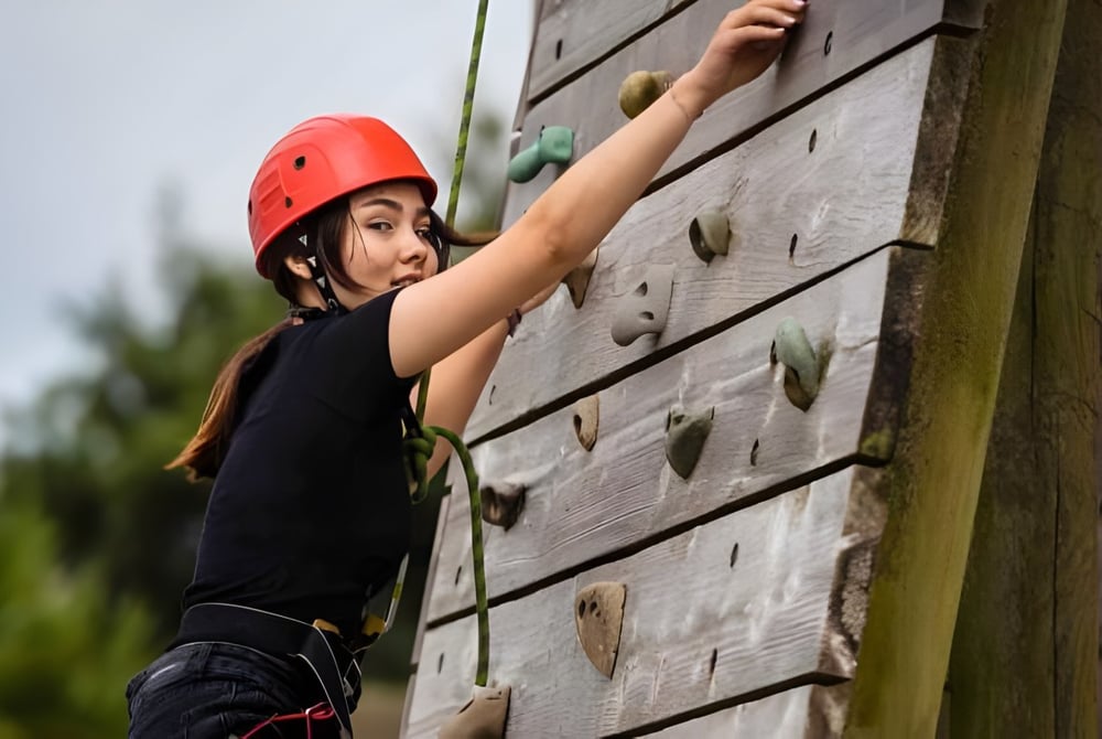 Ein Schüler der Westbourne School klettert mit rotem Helm an einer hölzernen Kletterwand im Außenbereich.