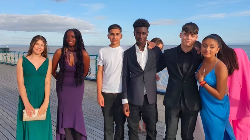 Eine Gruppe Schülerinnen und Schüler der Westbourne School steht auf einem Holzsteg mit Blick auf ein Gewässer unter bewölktem Himmel.