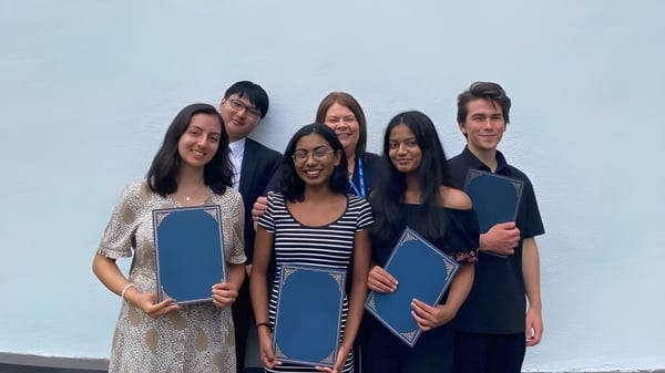 Eine Gruppe von Schülerinnen und Schülern der Westbourne School hält blaue Ordner vor einem hellblauen Hintergrund.