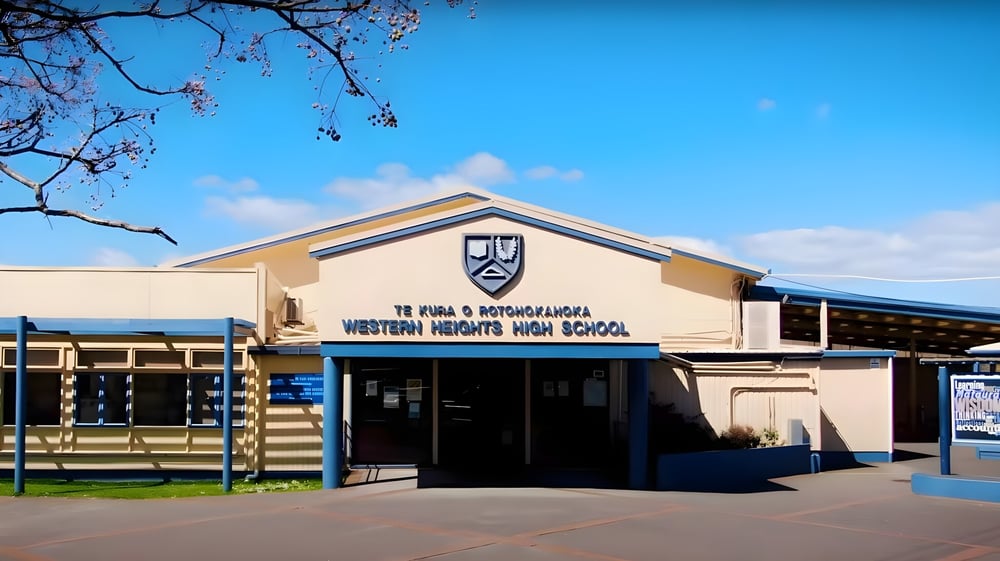 Das Gebäude der Western Heights High School steht unter einem blauen Himmel mit blühenden Bäumen im Hintergrund.