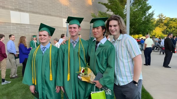 Eine Gruppe von Absolventen der Western Michigan Christian School steht in grünen Talaren und Mützen vor einem Backsteingebäude.