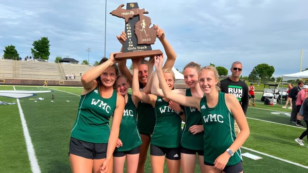 Schüler der Western Michigan Christian School feiern mit einem Pokal auf dem Sportfeld vor einem Stadion.