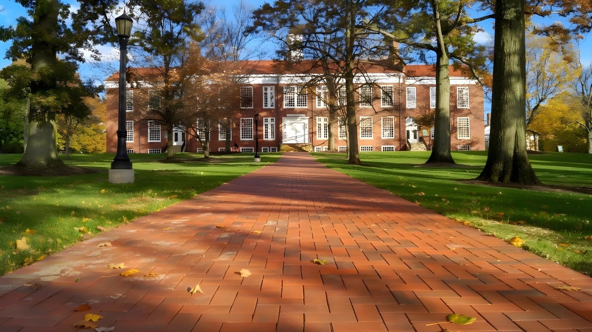 Ein gemauerter Weg verläuft durch den baumreichen Campus der Western Reserve Academy mit einem Backsteingebäude und herbstlicher Laubfärbung im Hintergrund.