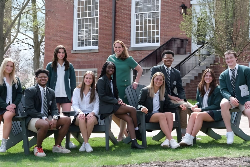 Eine Gruppe von Schülerinnen und Schülern sitzt vor einem Backsteingebäude auf den Stufen auf dem Campus der Western Reserve Academy.