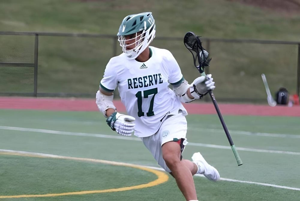 Ein Sportler mit einem weißen Trikot der Western Reserve Academy läuft mit einem Lacrosse-Schläger über das Spielfeld.