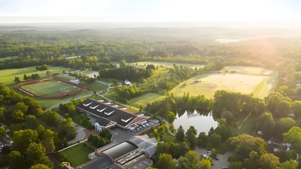 Die Western Reserve Academy zeigt eine Sportanlage mit Schulgebäuden und einem See inmitten eines bewaldeten Geländes.