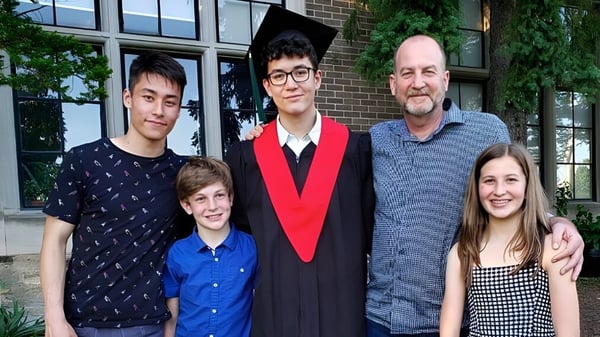 Eine Gruppe von Schülerinnen und Schülern der Western Technical-Commercial School posiert vor dem Backsteingebäude mit großen Fenstern nach der Graduation.