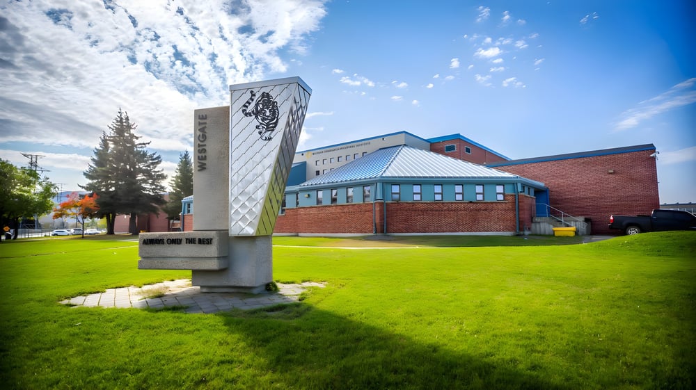 Das Westgate Collegiate & Vocational Institute zeigt einen dekorativen Monument auf dem Rasen vor einem Backsteingebäude mit hohem Turm.