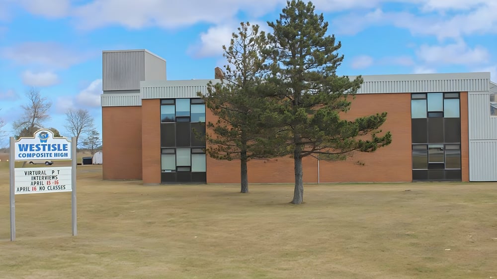 Das moderne mehrstöckige Gebäude der Westisle Composite High School mit einer großen Kiefer im Vordergrund vor blauem Himmel.