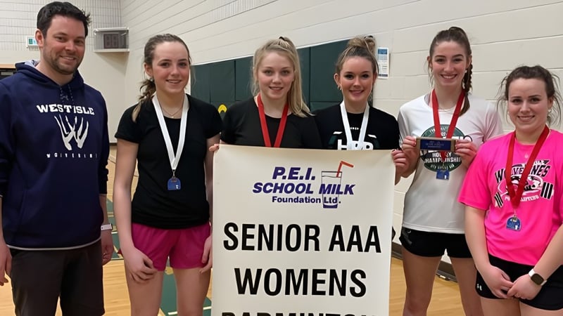 Eine Gruppe Schüler der Westisle Composite High School hält ein Banner für das Senior AAA Womens Event der P.E.I. School Milk Foundation in einer Turnhalle.