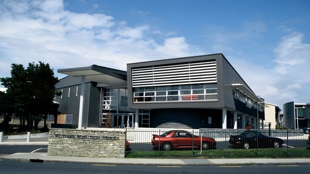 Das moderne, mehrstöckige Hauptgebäude der Westlake Boys High School mit umliegender Grünfläche und geparkten Autos.