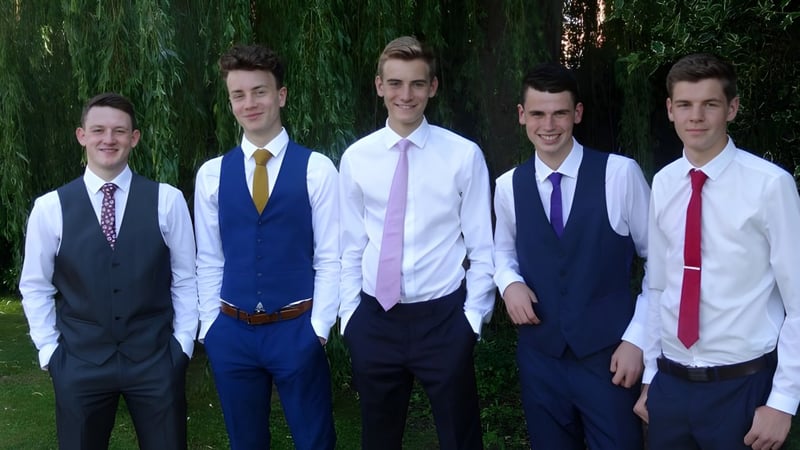 Eine Gruppe von fünf Jungen in formeller Kleidung steht auf dem Gelände der Westlake Boys High School vor grünen Bäumen.