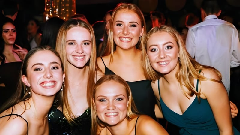 Schülerinnen der Westlake Girls High School posieren gemeinsam auf einer Feier mit bunter Beleuchtung im Hintergrund.