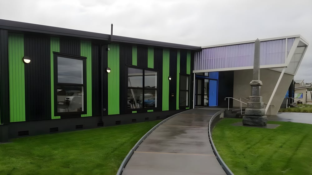 Das moderne grün-schwarze Gebäude der Westland High School mit gepflastertem Weg und Rasenfläche.