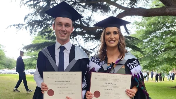 Zwei Absolventen der Westland High School in Talar halten ihre Zeugnisse in einem parkähnlichen Bereich.