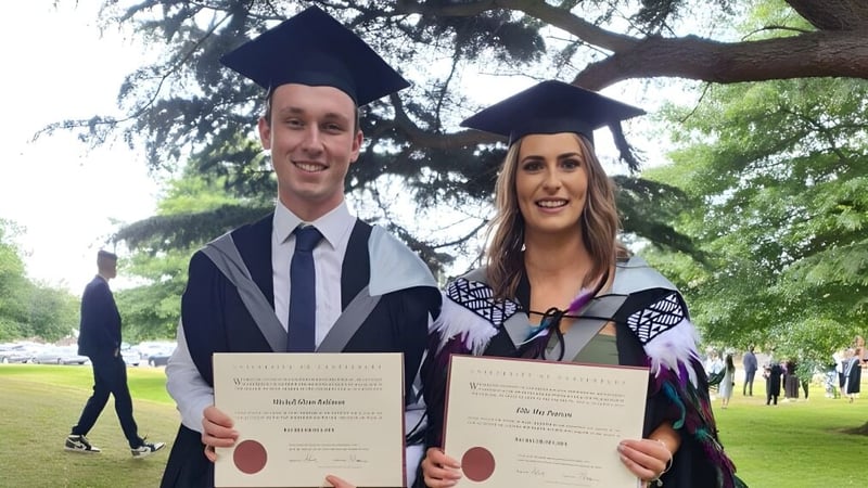 Zwei Absolventen der Westland High School in Talar halten ihre Zeugnisse in einem parkähnlichen Bereich.