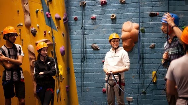 Schüler der Westminster School klettern mit Gurten und Helmen an einer bunten Kletterwand in der Kletterhalle.