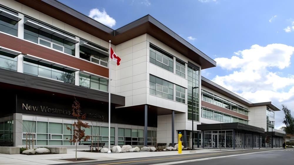 Das moderne mehrstöckige Gebäude der Westminster Secondary School mit Glasfassade und kanadischer Flagge unter bewölktem Himmel.