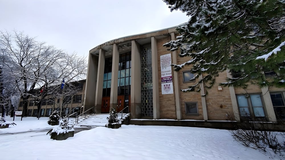 Das verschneite Gelände mit dem großen Steinbauwerk der Westmount High School im Winter mit kahlen Bäumen.